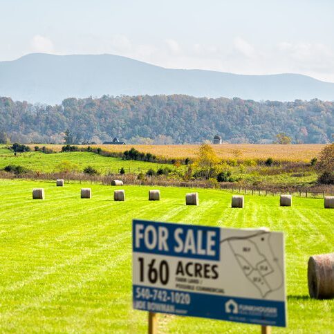 Hay roll bales on countryside field with sign for acres for sale